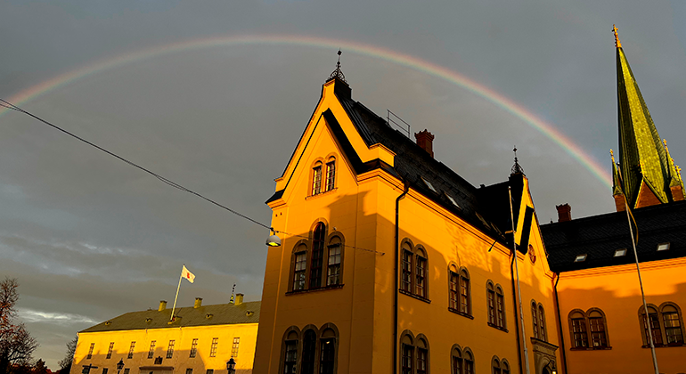 Fotografi på Linköpings stadshus och domkyrka med en regnbåge i bakgrunden