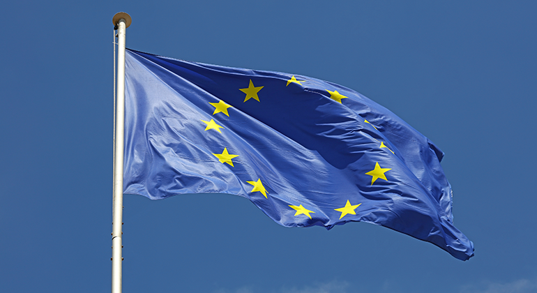 En närbild på den blåa EU-flaggan med gula stjärnor mot en klarblå himmel.