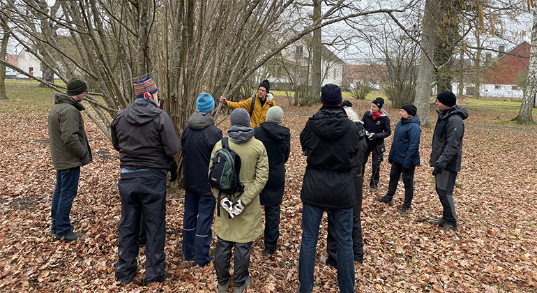 En grupp människor står framför en hassel och lyssnar på skogsträdgårdsmästaren Philipp Weiss.