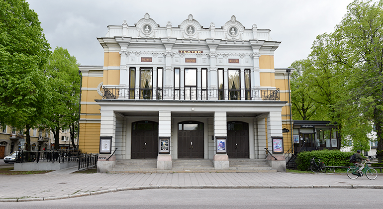 Gävle Teaters pampiga huvudentré med vita pelare, en stor balkong. Själva byggnaden är målad i gult.