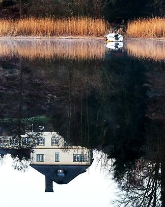 Reflektion i sjö där man ser huset speglas uppochnedvänt i vattnet. 