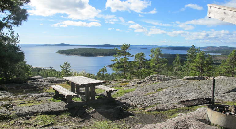 Foto av ett rastbord som står på en klippa framför en utsikt mot havet och några öar.