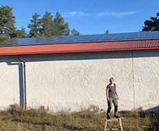 En kvinna står på en stege framför en stor byggnad med solceller på taket. Foto.