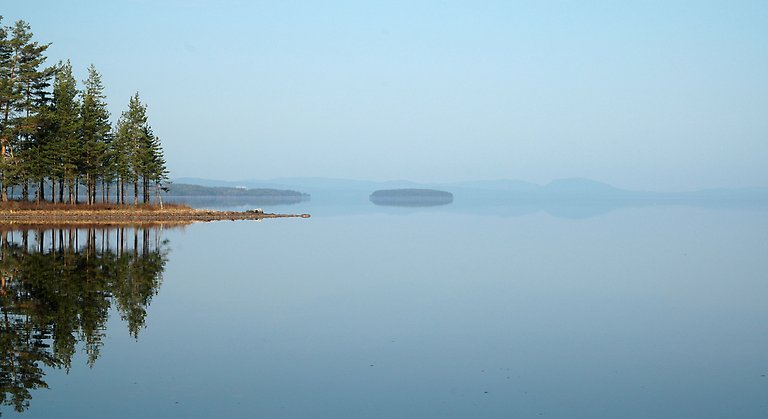 Blått stilla vatten med en ö långt borta i horisonten