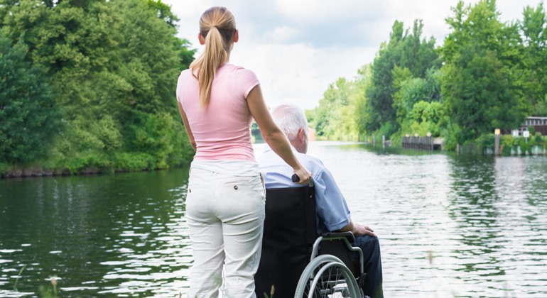 Kvinna med äldre man i rullstol tittar ut över sjön.