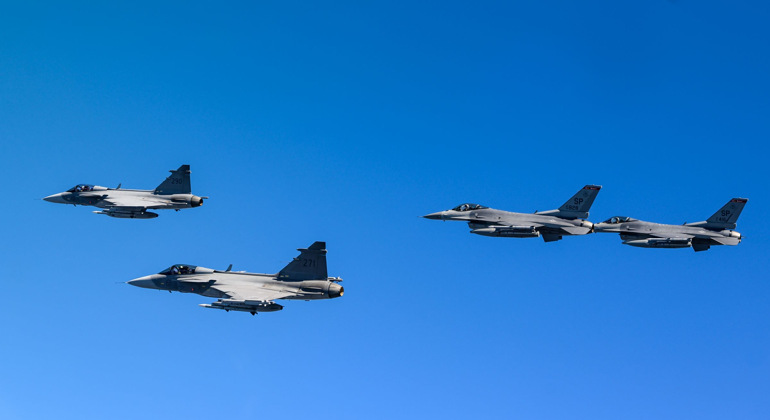 Fyra stridsflygplan flyger mot en blå himmel. Två är JAS Gripen och två är F 16.