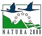 Symbolen för Natura 2000. Två mörkblå gås-liknande fåglar flyger över gröna berg. Mellan fåglarna och bergen finns sju ofyllda stjärnor i en halvcirkel. Längst ner texten: NATURA 2000.