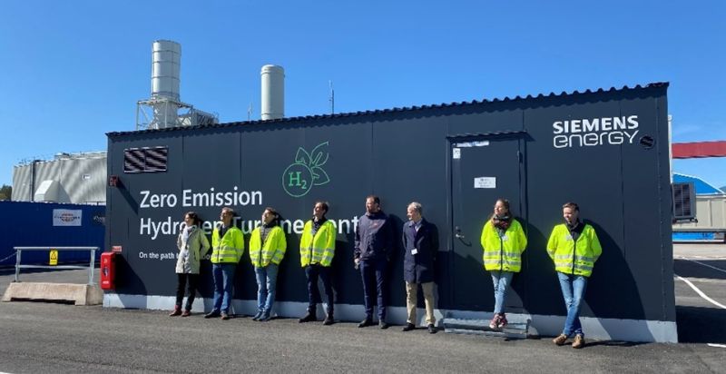 åtta personer som står i solen mot en container som det står Siemens energy på. 