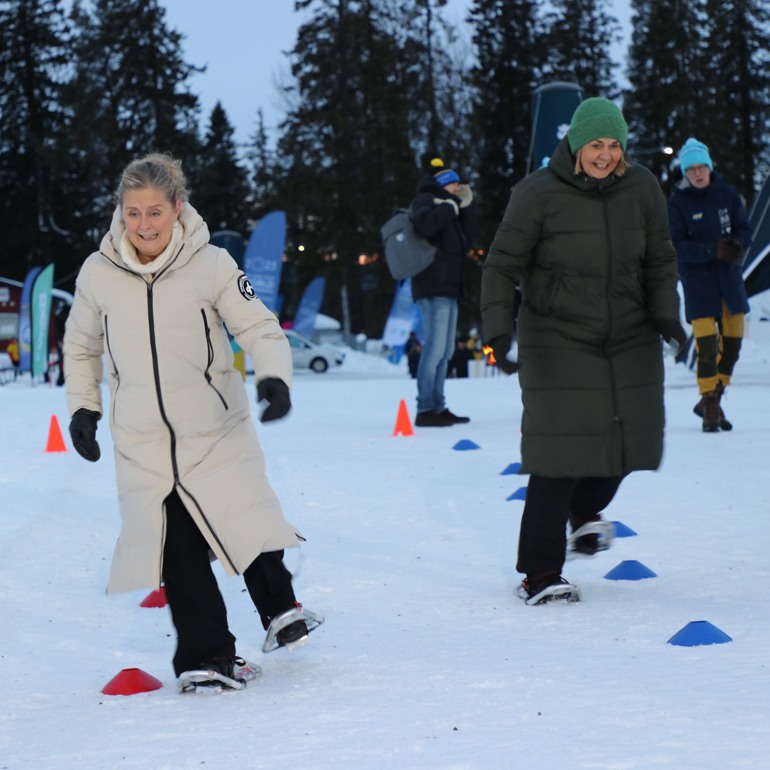 Två kvinnor springer mot kameran. De är Anne-Li Sjölund, idrottspolitisk talesperson i Centerpartiet. Hon sitter i riksdagen och tävlade mot landshövding Marita Ljung i löpning med snöskor. Loppet slutade oavgjort.