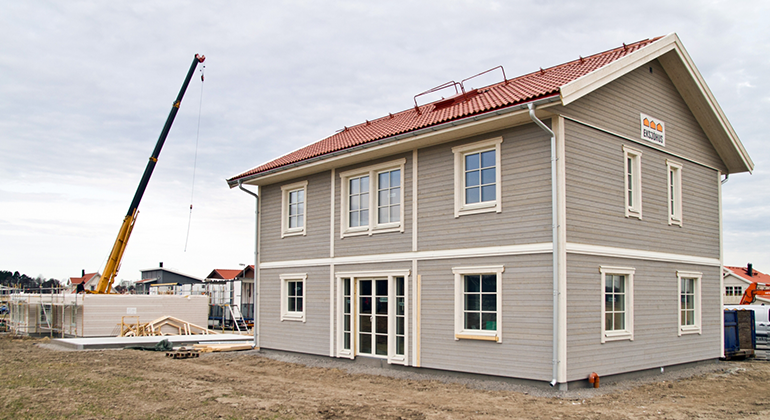 Bild på nybyggt hus i villaområde, med en lyftkran i vänstra delen av bilden där ännu ett hus ska byggas. 