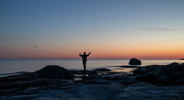 En flugfiskare i silhuett vid en solnedgång vid havet. Fotograf är Lars Molander.