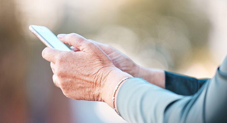 Närbild på äldre kvinna som håller i en mobiltelefon.