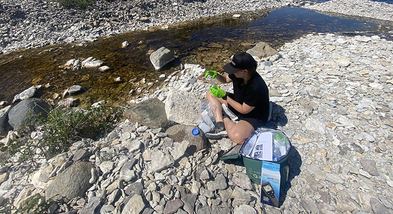 En kvinna sitter på en strand och häller upp vattenprov i provtagningsutrustning.