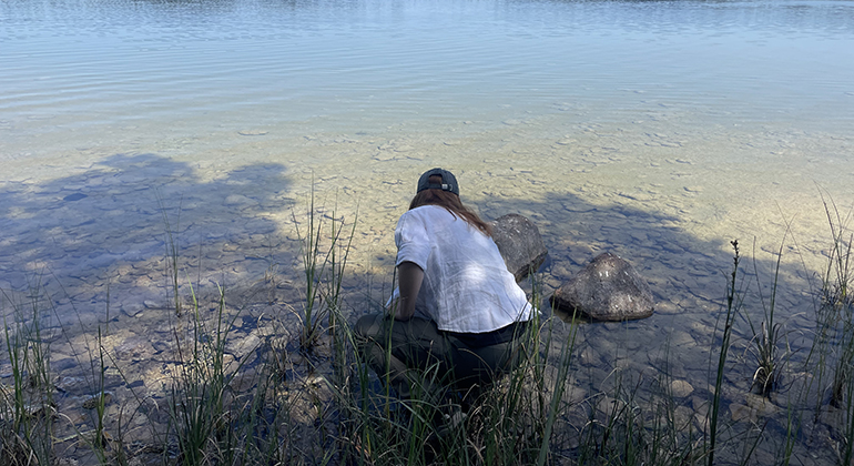 En kvinna lutar sig ner för att ta ett vattenprov från en sjö.