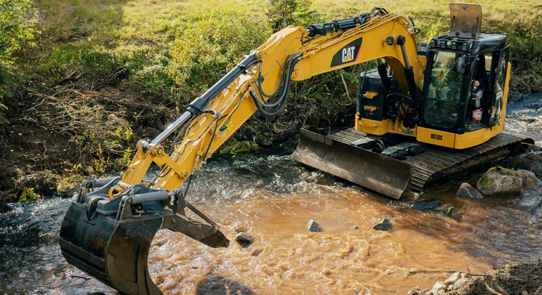 En bulldozer som gräver sig fram genom en lerig bäck.