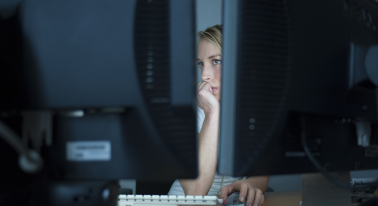 Kvinna sitter delvis gömd bakom två stora datorskärmar. 