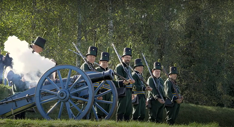 Kanonen avfyras vid Eda skansar. En grupp män står uppställda invid kanonen, utklädda till gammaldags soldater.