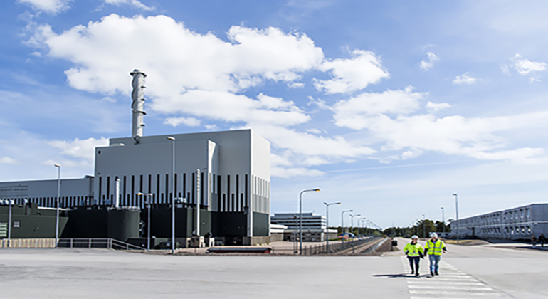 Kärnkraftverket i Oskarshamn med stora reaktorbyggnaden och ett par personer som går på området framför.