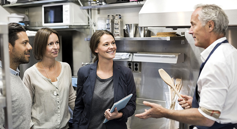 Livsmedelsinspektörer står och pratar med en kock i restaurang köket