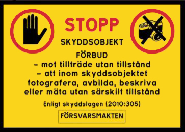 Stoppskylt med texten Stopp. Skyddsobjekt förbud - mot tillträde utan tillstånd - att inom skyddsobjektet fotografera, avbilda, beskriva eller mäta utan särskilt tillstånd. Enligt skyddslagen (2010:305). Försvarsmakten.