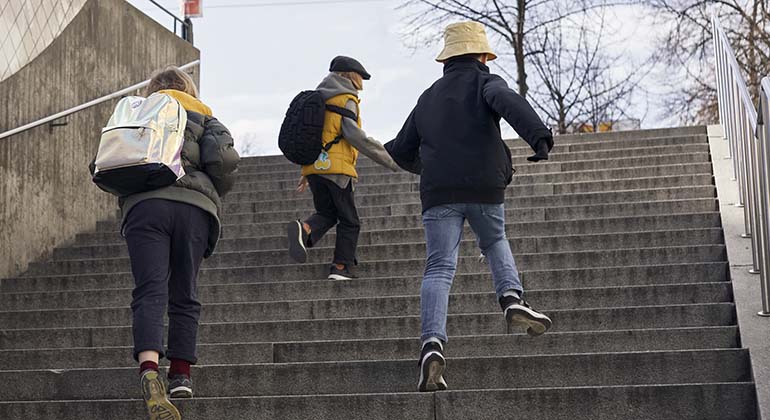 Tre barn som springer uppför en trappa utomhus.