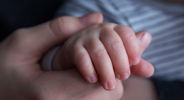 Närbild på en vuxen hand som håller en barnhand. Foto: Unsplash.