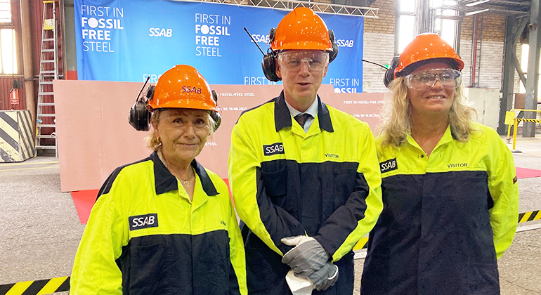 Tre personer, Beatrice Ask, Urban Granström och Catharina Fredriksson, står med gula varseljackor samt hjälmar inne i en industrilokal på SSAB.