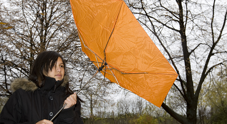 Person med paraply som vänder sig efter vinden under regnoväder.