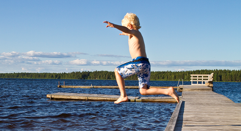 Pojke hoppar från brygga ner i en sjö.