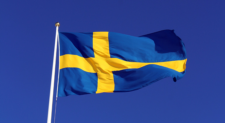 Svenska flaggan, ett gult kors på blå botten, mot klarblå himmel.