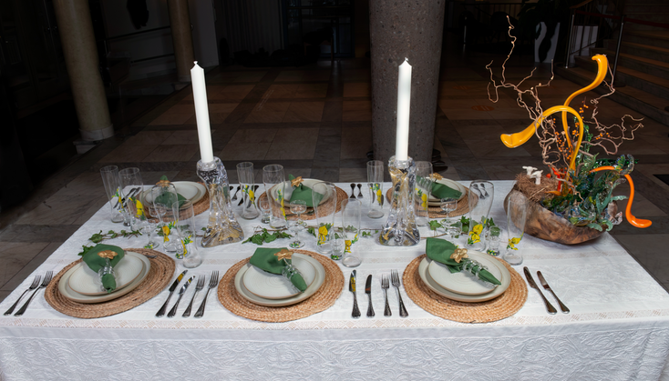 Ett uppdukat bord för sex personer, med tallrikar, bestick, ljus och konstnärlig utsmyckning.