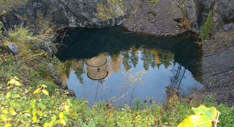 Ett vattenfyllt gruvhål där en rund tornliknande byggnad speglas i vattenytan.