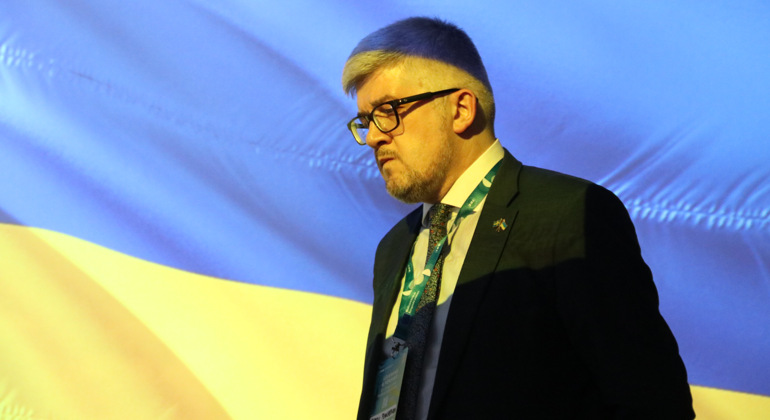 Ukrainas Sverige-ambassadör Andrii Plakhotniuk på scenen med blågul bakgrund.