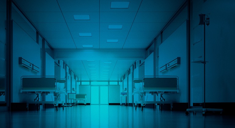 En sjukhuskorridor med tomma sjukhussängar i blått ljus. 
