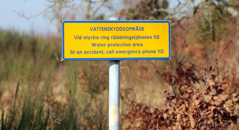 Skylt med information om att marken är ett vattenskyddsområde och att man ska ringa 112 vid en olycka.