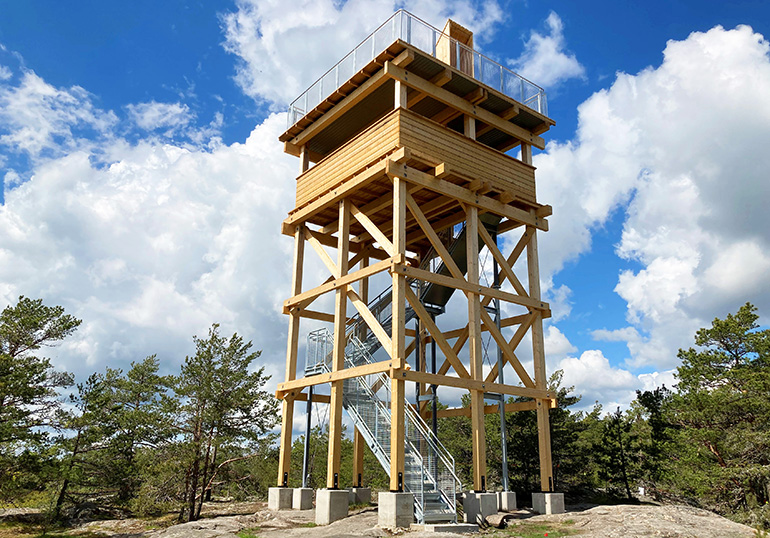 Utsiktstornet står på ett berg med skog runt omkring, tornet består två plan i trä och en trappa i stål. 