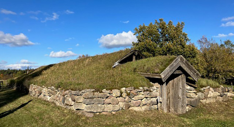 Ett lågt hus byggt i staplad sten med gräs på taket. En dörr finns på gaveln, inga fönster syns.