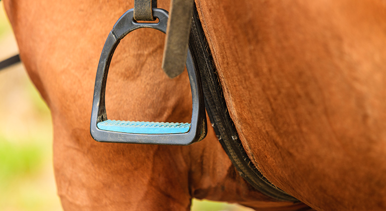 Närbild på brun häst där en hängande stigbygel och sadeljorden är i fokus.
