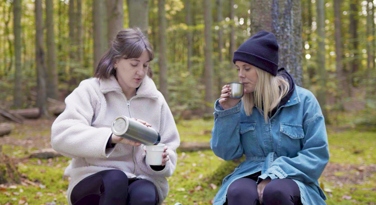 Två personen dricker kaffe i skogen.