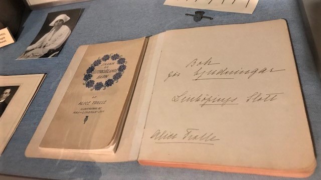 Historisk anteckningsbok utställd på museum. I boken är det skrivet "Bok för bjudningar Linköpings slott. Alice Trolle". I det övre vänstra hörnet är det en svartvit bild på Alice Trolle.