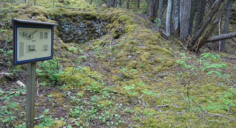 En gammal stenlämning, resterna av en ugn, syns på marken i skogen.