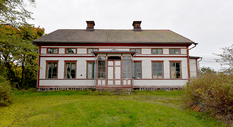 Huset är målat i en ljus färg med röda inramningar såsom på knuten av huset och runt fönstren.