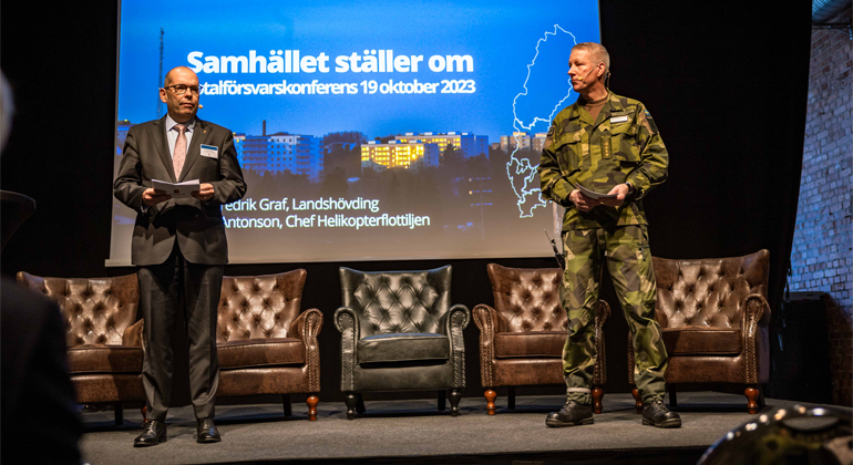 Landshövding Carl Fredrik Graf och överste Mats Antonsson, chef för försvarsmaktens helikopterflottilj står på en scen och pratar