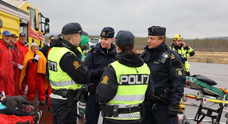 Bild på svenska och norska poliser i samspråk vid Sälens flygplatsen. I Bakgrunden skymtar ambulanspersonal och statister i övningen. 