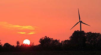 Siluetten av ett vindkraftverk syns mot solnedgången.