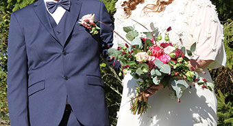Ett uppklätt par visas från halsen nedåt. Den ena har kostym, den andra en vit klänning och håller i en blombukett.