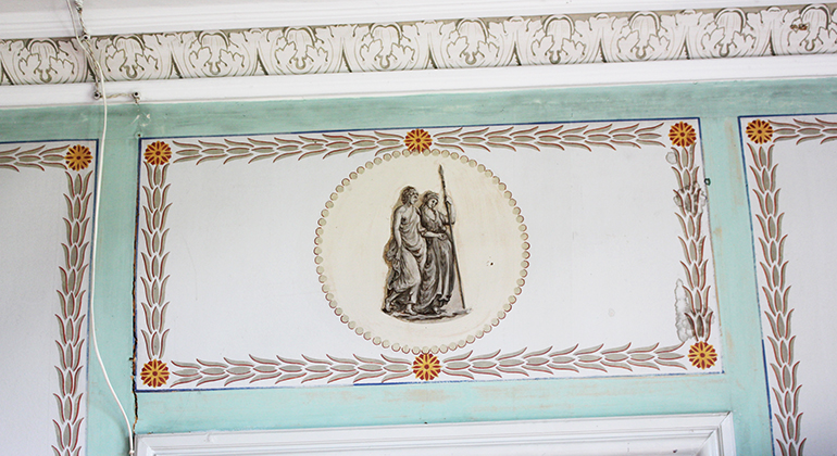 En målning ovanför dörrposten med två personer av äldre motiv.