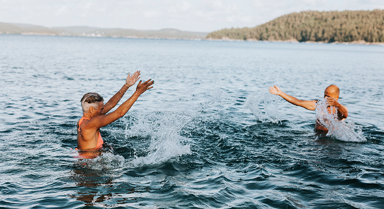 Bilden visar en man och en kvinna som svalkar sig och stänker vatten på varandra i en sjö en varm sommardag.