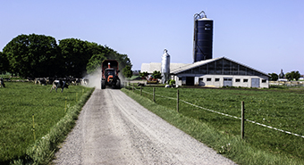 traktor på grusväg omgiven av åker och en gård på höger sida