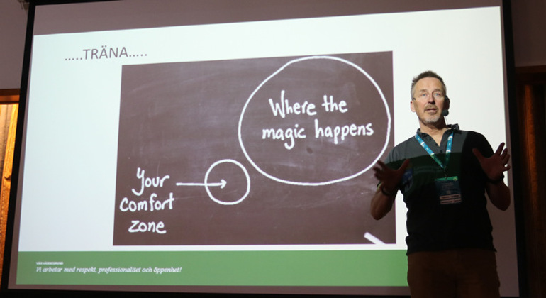 Man står framför en stor projektorduk som visar en liten texten "Your comfort zone" och "Where the magic happens".